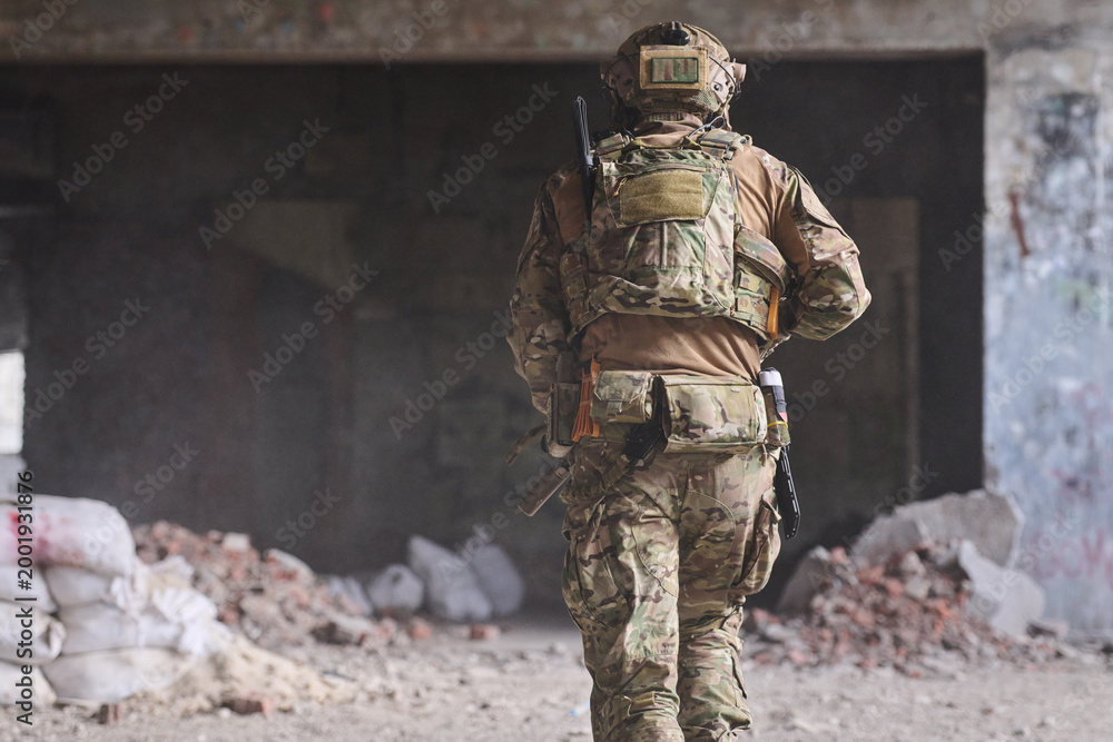 Fototapeta premium Military Soldier in Camouflage Gear Moving Through Abandoned Urban Building During Tactical Operation
