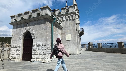 Young woman with a backpack exploring the famous swallow's nest castle, a historic landmark and popular tourist attraction situated on the aurora cliff overlooking the black sea in crimea