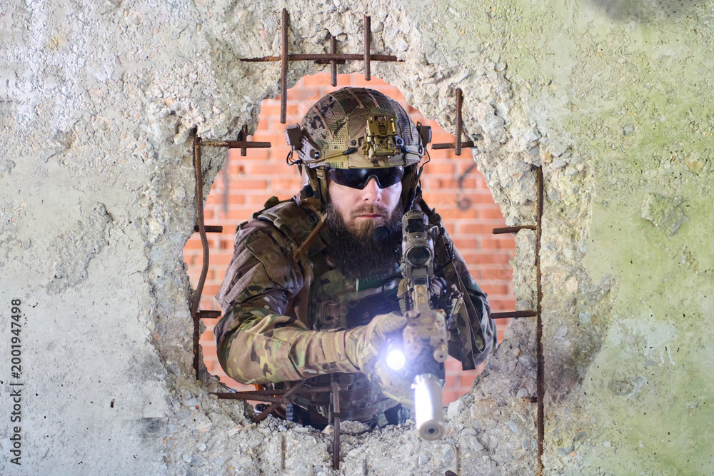 Obraz premium Tactical Soldier With Rifle Pointing Through Bullet-Hole Wall During Urban Combat Training