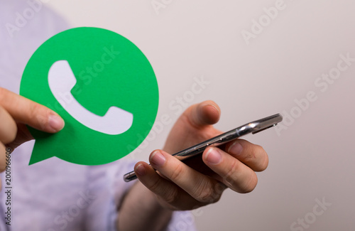 Person holding a Whatsapp icon and a mobile phone. Concept of online messaging, connection, and mobi