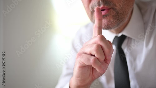 Professional man in formal attire holding a finger to his lips, expressing secrecy or confidentiality. 4K.