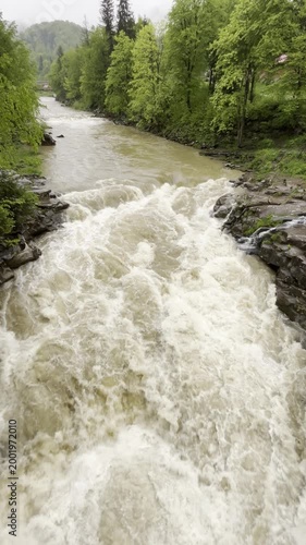 A river flows rapidly through a wooded area, showcasing strong currents and lush greenery