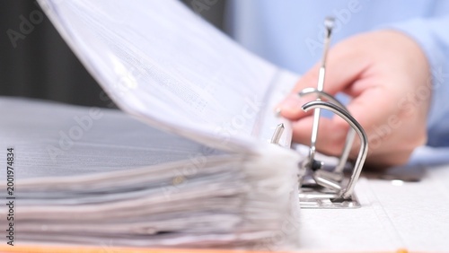 Quadro su tela Hand flipping through paperwork in a ring binder on an office desk, organizing b