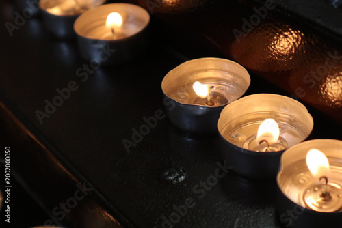 Foto File di candele tealight accese in una chiesa, fiammelle votive disposte ordinat