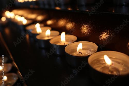 Fotografía File di candele tealight accese in una chiesa, fiammelle votive disposte ordinat