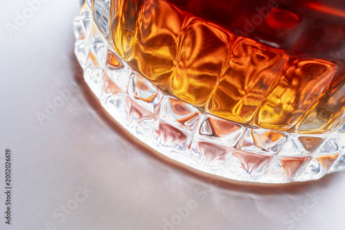 Crystal whiskey glass macro detail with ice and amber liquid on minimal light background