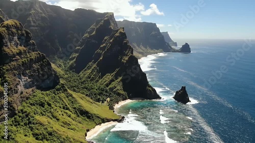 An aerial view showcases a dramatic coastline with lush green cliffs plunging into the turquoise waters of the Pacific Ocean, highlighting the raw beauty of a remote island landscape.