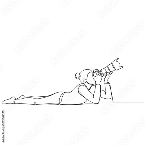 One line drawing of female photographer lying on ground capturing photos with professional dslr camera for creative work.