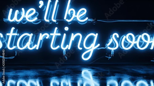A vibrant blue neon sign displaying the message 'we'll be starting soon' is reflected in a dark, glossy surface, creating a captivating and futuristic aesthetic.
