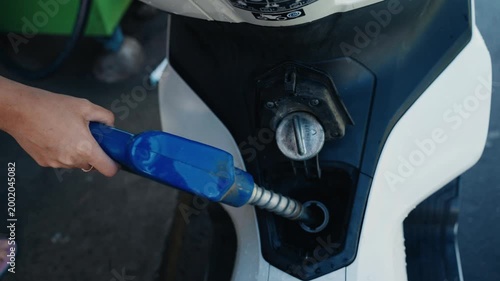 Person refueling a white scooter at a gas station