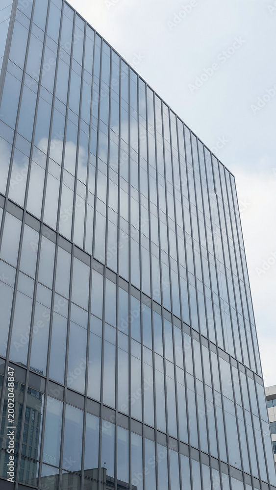 Naklejka premium Modern Glass Office Building Facade Reflecting Soft White Clouds Low Angle