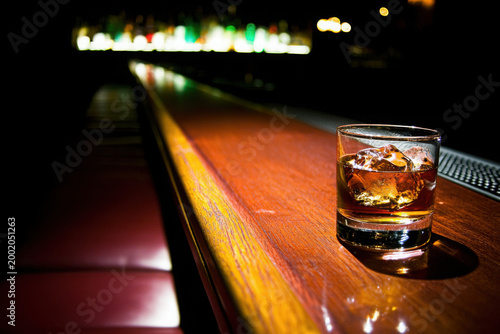 Glass of whiskey with ice on bar counter in dimly lit lounge
