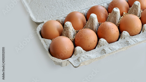 High-priced groceries. Expensive eggs conceptual visual. Brown eggs in an open cardboard box, a gold chain on top. Conceptual image, rising food prices, inflation, economic crisis