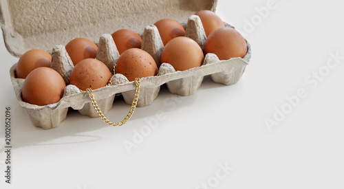 High-priced groceries. Expensive eggs conceptual visual. Brown eggs in an open cardboard box, a gold chain on top. Conceptual image, rising food prices, inflation, economic crisis