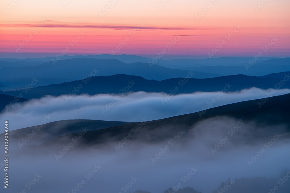 Fototapeta premium Sunset over mountains covered in misty clouds