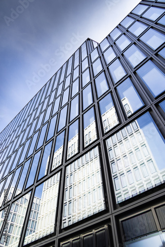 Modern office building reflects blue sky and city skyline during daytime in urban setting