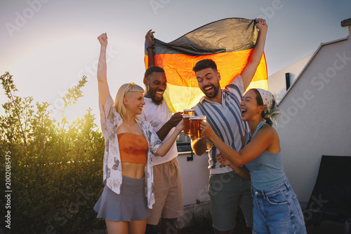 Group of diverse friends cheering and toasting beer outdoors with a german flag