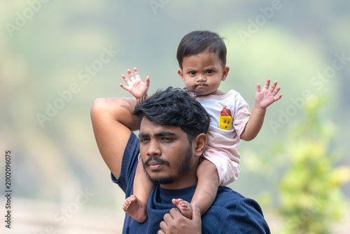 A man carries a child on his shoulders as they look ahead, enjoying time outdoors together