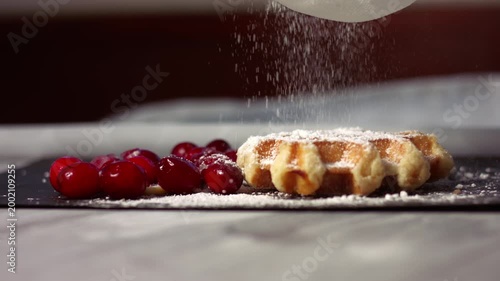 Sprinkling dusting of sugar on waffles with ripe cranberries
