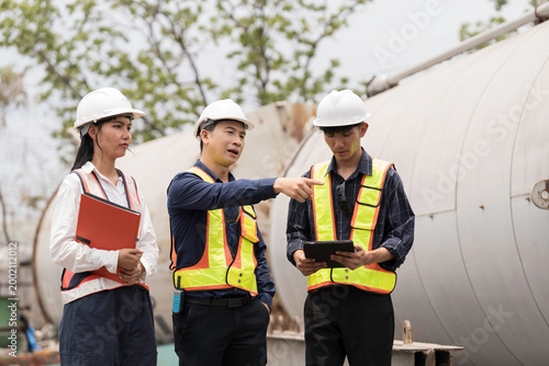 Old chemical tanks. Temporary storage of liquid chemicals at container yard. Asian industrial workers in safety gear discussion and checking old chemical storage tanks at container yard