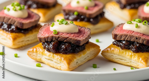 Gourmet beef tenderloin appetizers served on flaky puff pastry with savory onion jam and a dollop of sauce