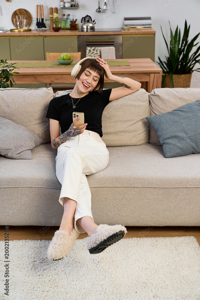 Fototapeta premium Young beautiful woman enjoys a relaxing moment at home while using her phone and smiling