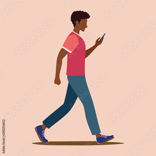 Young man walking while looking at his smartphone in a pink shirt and blue jeans on a light pink background