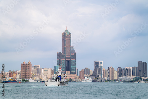 A view of the Kaohsiung port skyline featuring the iconic 85 Sky Tower, with a patrol boat sailing on the water during a summer afternoon in Taiwan.