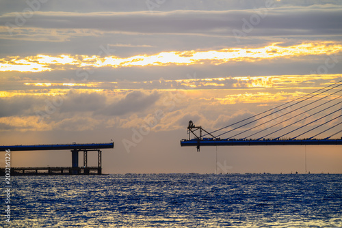 A scenic view of the Danjiang Bridge under construction in New Taipei City, Taiwan, captured during a vibrant summer sunset over the ocean.