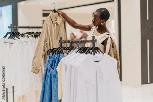 Фотография Stylish African American Woman Choosing Clothes in Modern Fashion Boutique