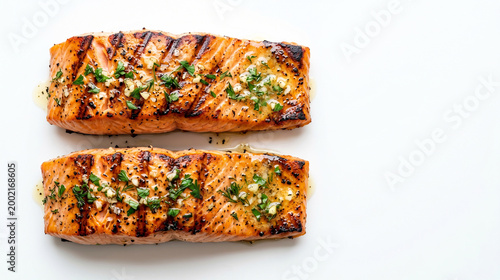 Top view of two grilled salmon fillets with garlic butter and herbs on a white background with copy space for text. High-end commercial food photography
