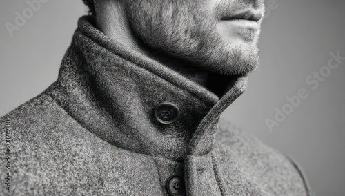 Dapper Profile in Monochrome: A man in a sophisticated coat poses with poised elegance, his style radiates an air of classic charm and subtle sophistication.