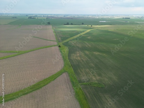 Artful farm fields show the difference in planting times in difference fields with a buffer strip flying high above rural Illinois farm fields. Drone, flying