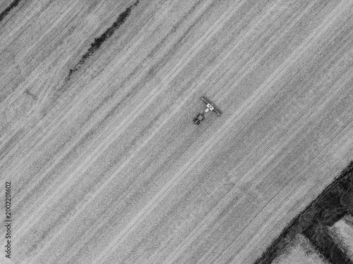 From way up high in a drone looking down on a tractor and planter in a field shot in a black and white art texture method. Making farming look like a work of art.