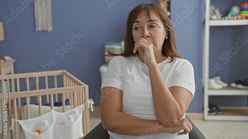 Tableau sur toile Woman finger to lips for silence in baby room next to wooden crib, toys, storage pockets and chair; pensive maternal