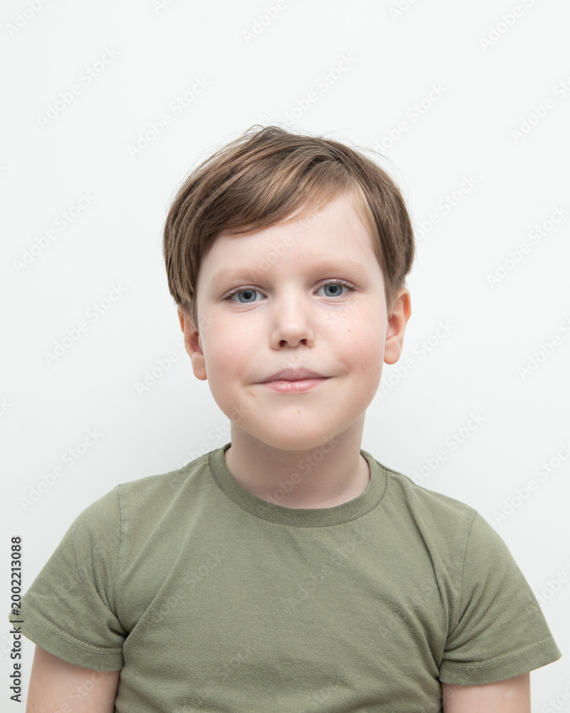 Fototapeta premium An emotional boy stands in a green T-shirt on a white background