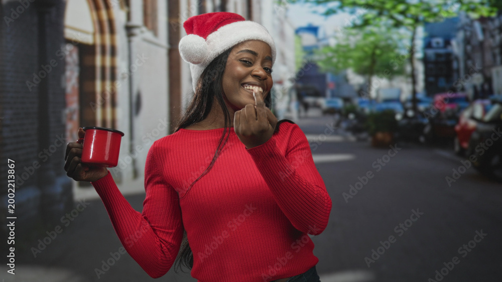 Obraz premium Woman in santa hat holding red mug and showing middle finger on a street lined with parked cars and trees, smiling broadly; mischievous.