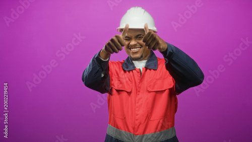 Bilde på lerret Man construction worker in hard hat and red uniform makes ok signs with both hands in studio; cheerful confidence