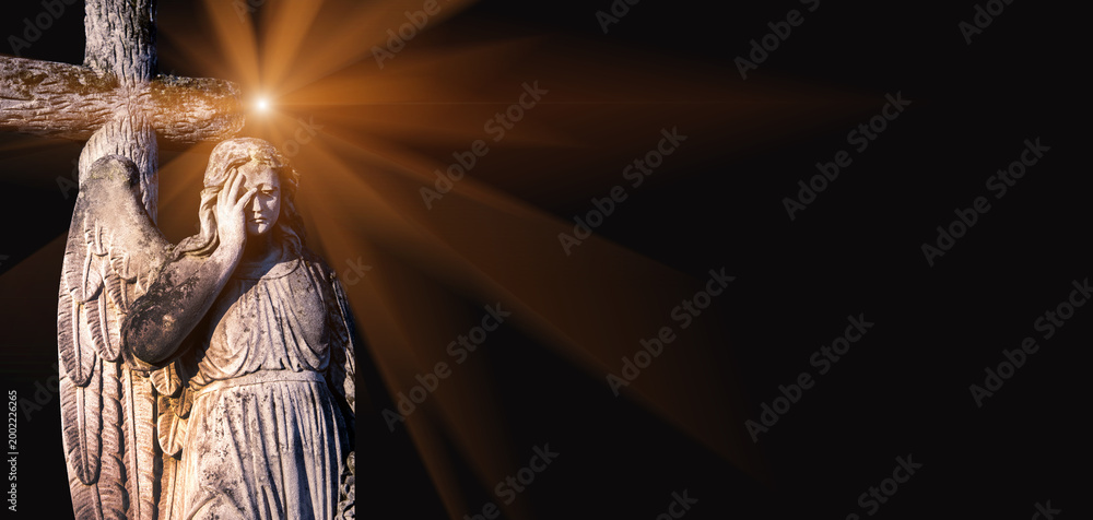 Fototapeta premium sad angel statue with cross and dramatic light rays on black background