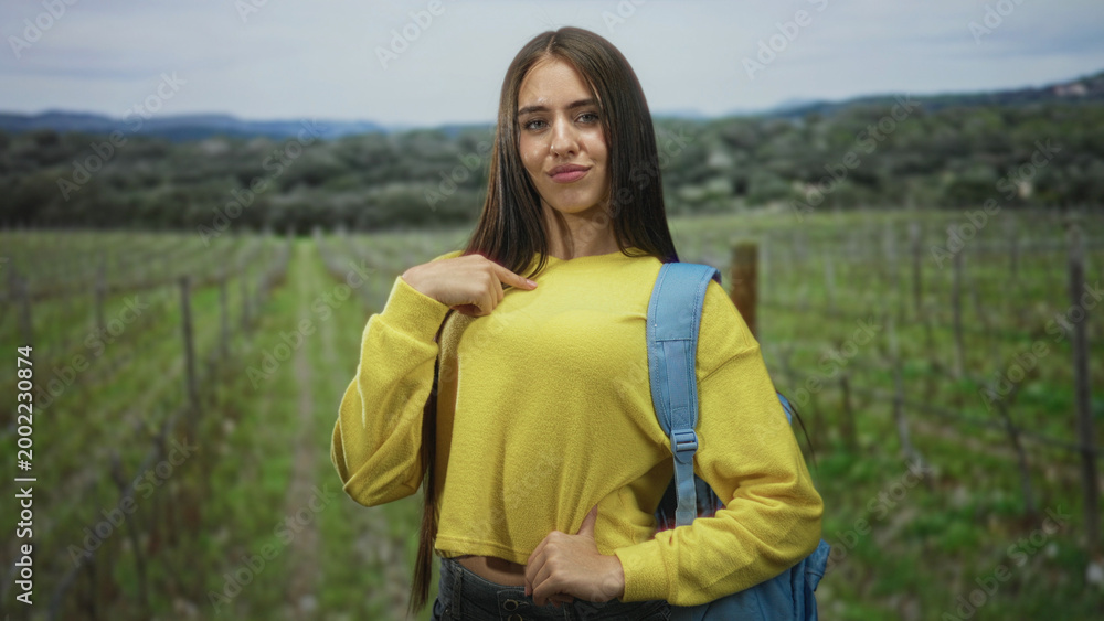 Naklejka premium Student points finger to chest wearing yellow sweater and blue backpack in forest; confidence independence youth.