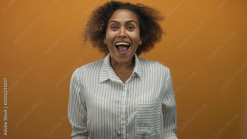 Fototapeta premium Woman clapping hands in studio with orange wall and striped shirt visible from chest up; joy celebration.