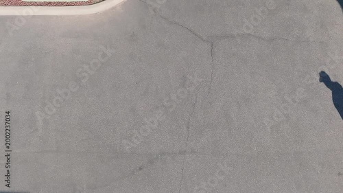 Overhead shot of a man slowly walking on a concrete sidewalk, with his shadow taking the main focus of clip. 
