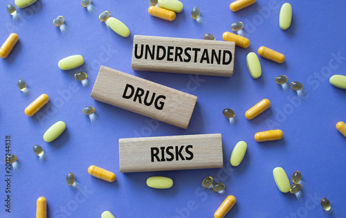 UNDERSTAND DRUG RISKS symbol. Concept words UNDERSTAND DRUG RISKS on wooden blocks. Beautiful purple background with pills. Healthcare and UNDERSTAND DRUG RISKS concept. Copy space.