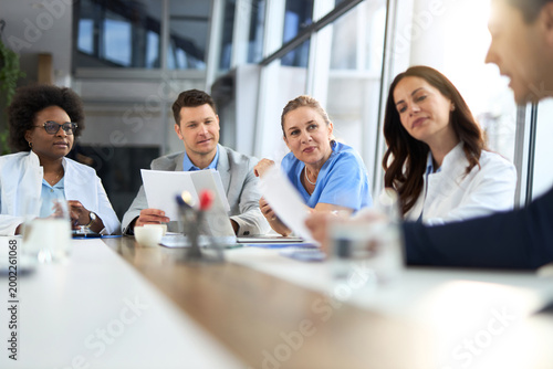 Team of doctors and two businessmen going through paperwork in a hospital.