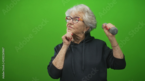 Cuadro en lienzo Senior woman holds dumbbell in right hand and rests chin on left hand in studio; confidence strength wellbeing