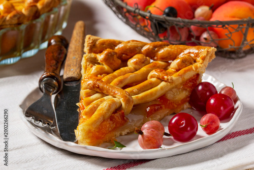 Apricot pie decorated with dough ornament and a metal basket with fruits and berries.