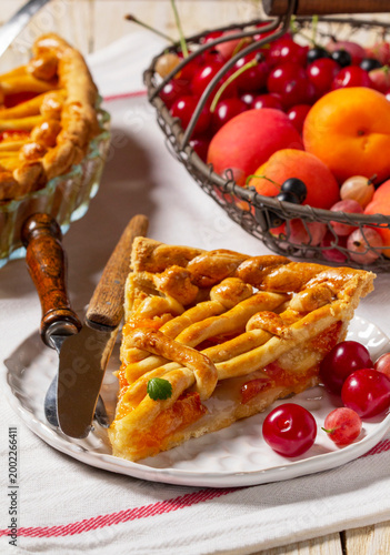 Apricot pie decorated with dough ornament and a metal basket with fruits and berries.