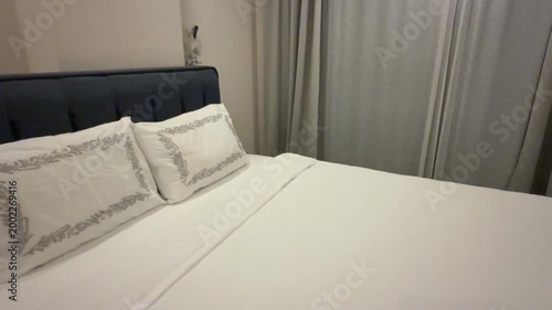 Cozy bedroom with neatly arranged bed, white pillows, and soft gray curtains creating a calm background