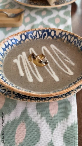 Bowl of creamy mushroom soup with drizzle served in patterned dishware on decorative fabric