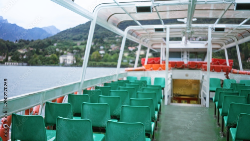 Obraz premium Defocused ferry deck with rows of green seats and distant lake and mountains, blurred outdoor; template overlay virtual production.